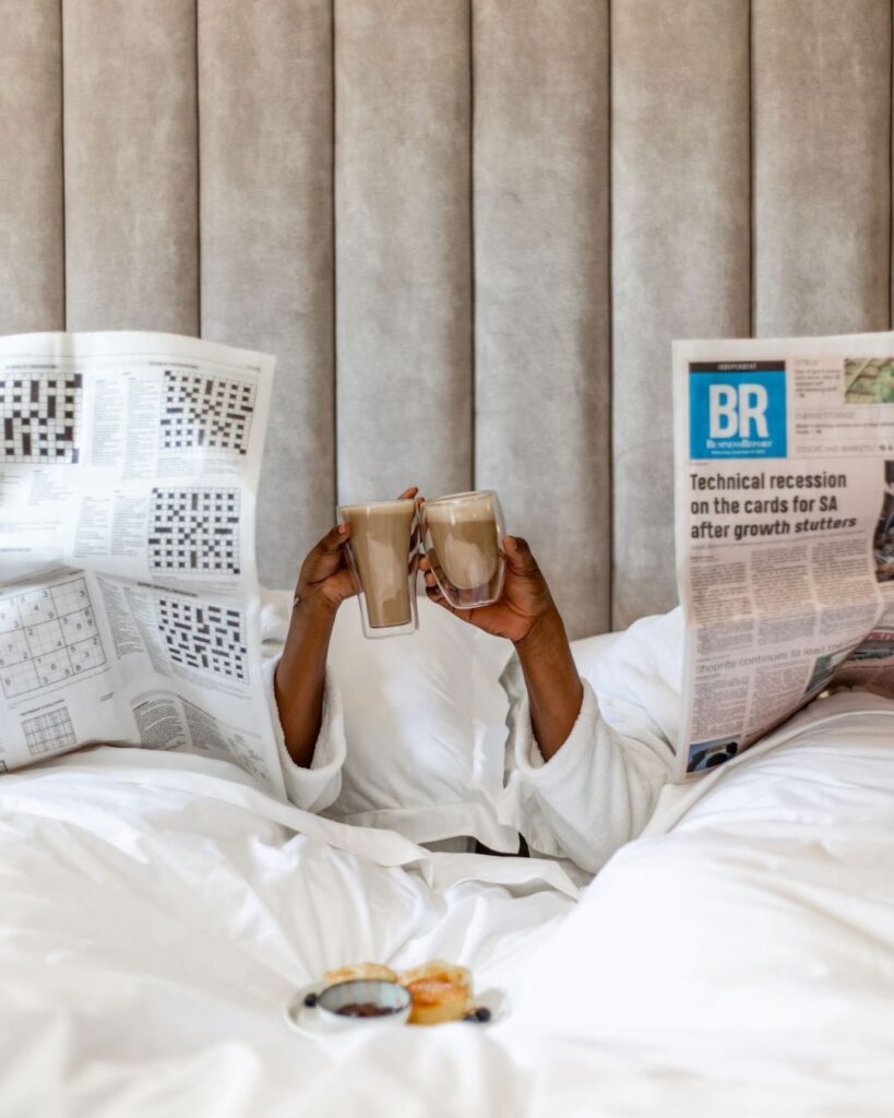 A couple in bed with coffee and a newspaper at Sanctuary Mandela